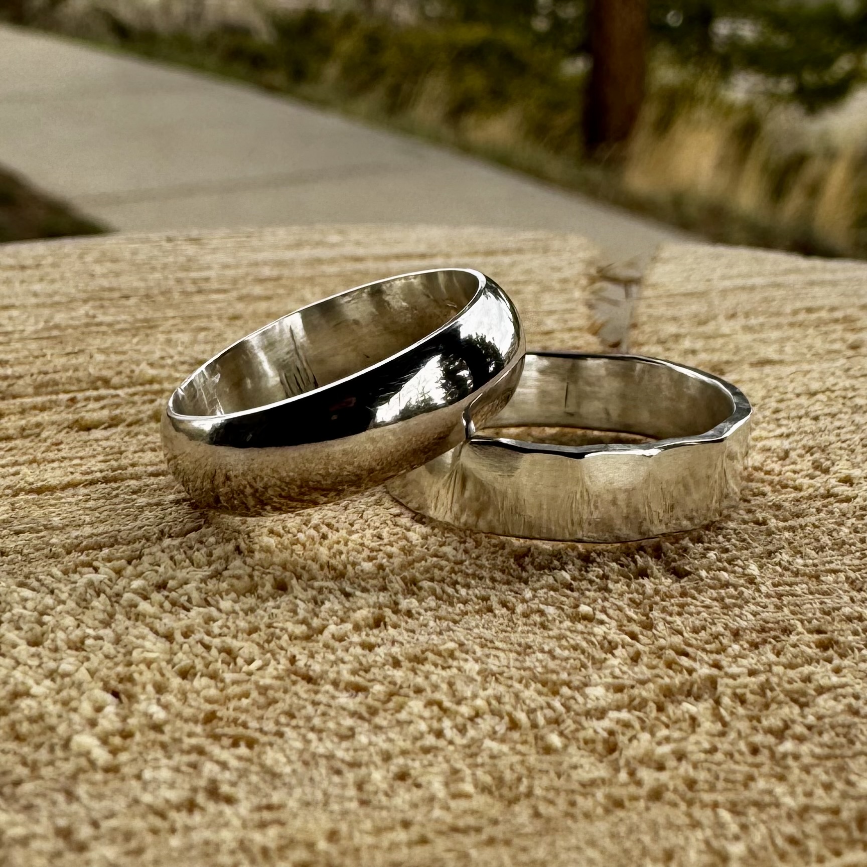Handcrafted silver rings resting on a textured wood surface outdoors
