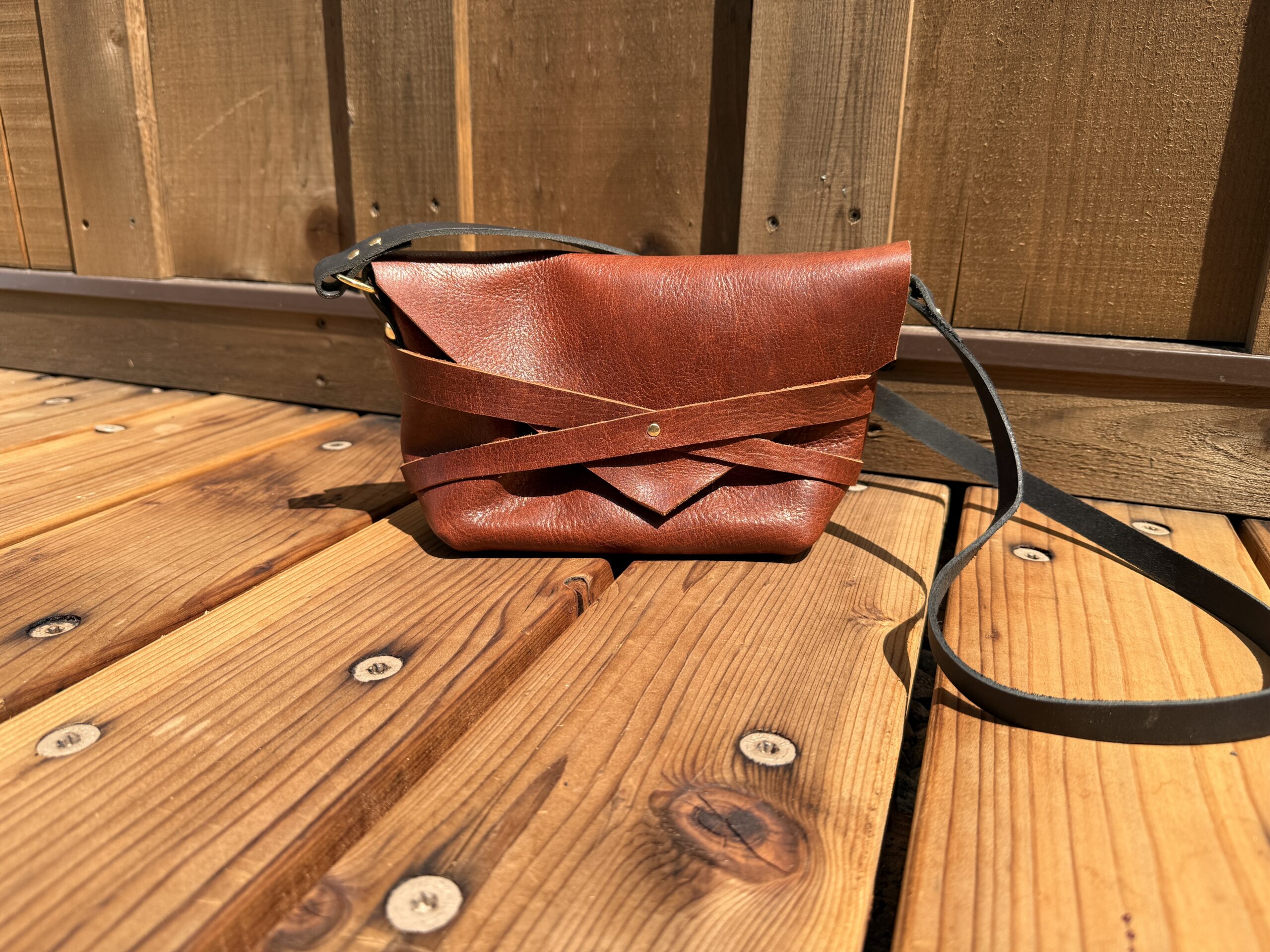 Handmade brown leather crossbody bag with woven leather detail and adjustable strap, created during a leatherworking workshop.