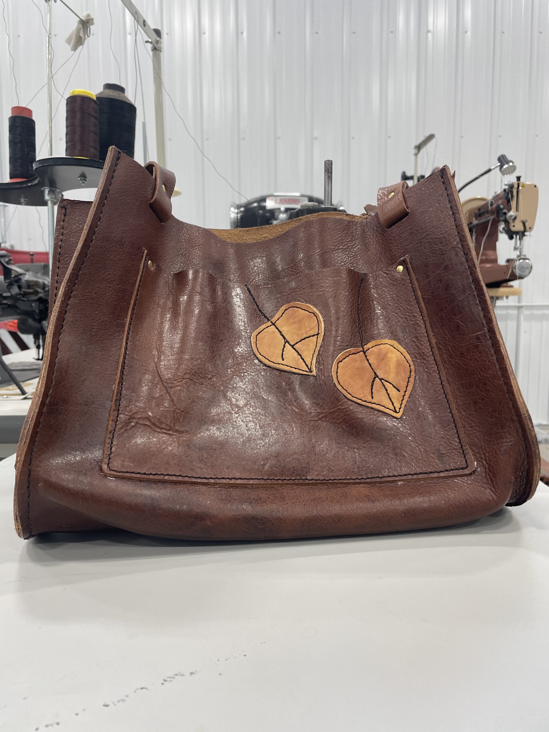 Handmade brown leather tote bag with stitched leaf appliqués, created using traditional leatherworking techniques.