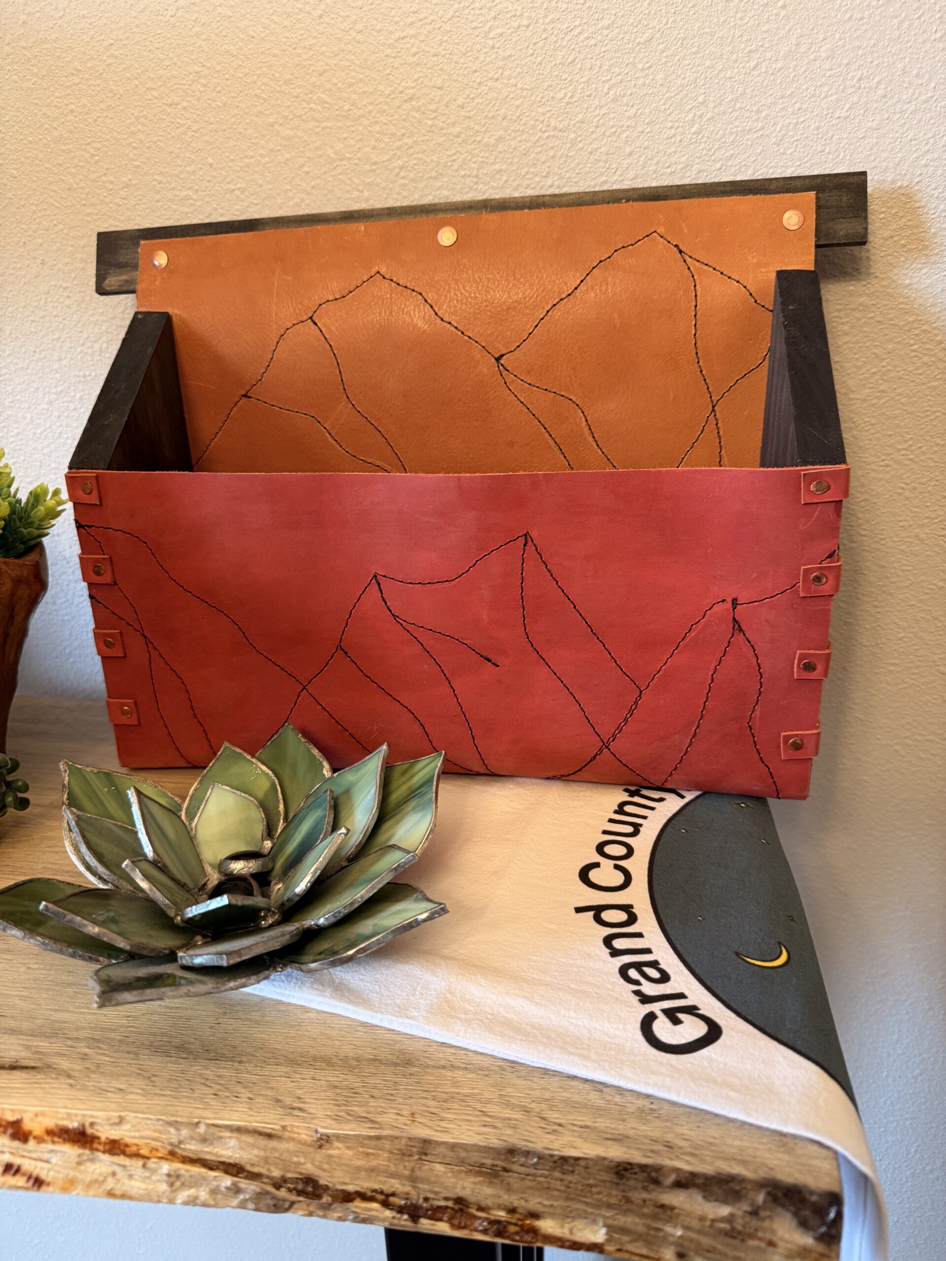 Handcrafted red and orange leather wall organizer with mountain stitching and wooden frame, created for a Rocky Mountain Folk School workshop in Grand Lake, Colorado.