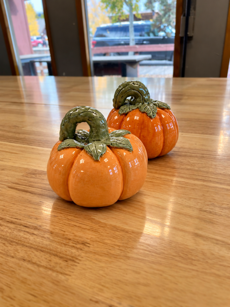 Two handmade glazed ceramic pumpkins with orange bodies and green stems, examples from a fall pottery workshop at Rocky Mountain Folk School in Grand Lake, Colorado.